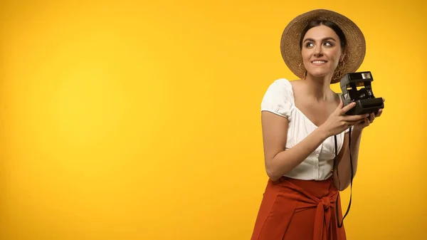 Cheerful tourist in straw hat holding vintage camera isolated on yellow — Foto stock