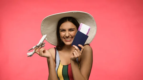 Щаслива жінка в купальнику тримає іграшковий літак і паспорт ізольовані на рожевому — стокове фото