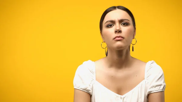 Skeptical woman in blouse and earrings looking at camera isolated on yellow — стоковое фото