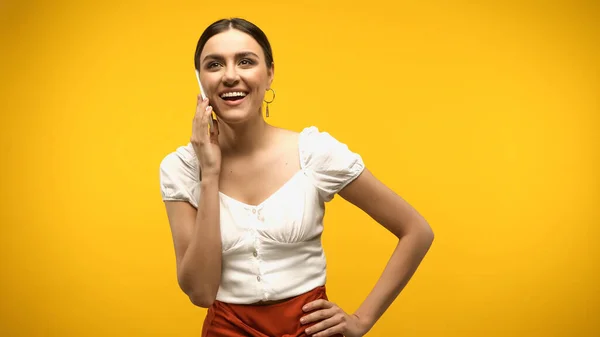 Happy woman in blouse talking on smartphone isolated on yellow — стоковое фото