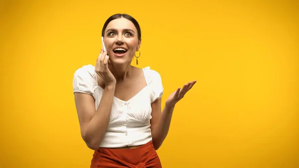 Young brunette woman talking on cellphone isolated on yellow — Stockfoto