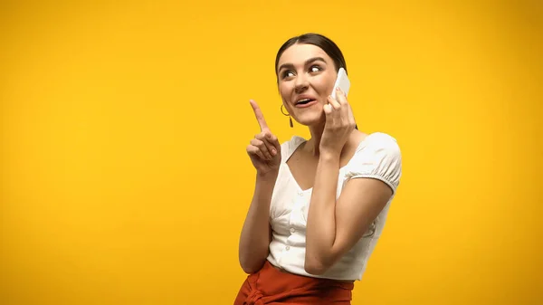 Mulher morena falando no celular e tendo ideia isolada no amarelo — Fotografia de Stock