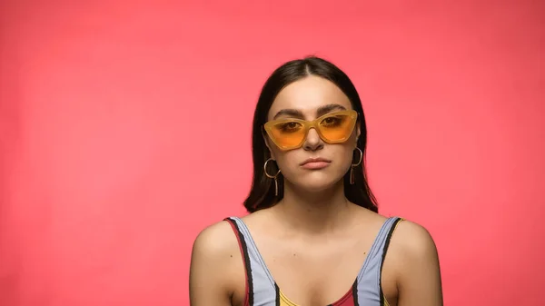 Triste femme en lunettes de soleil et maillot de bain regardant la caméra isolée sur rose — Photo de stock