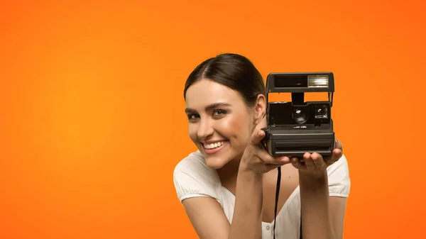 Усміхнена жінка тримає старовинну камеру ізольовано на помаранчевому — стокове фото