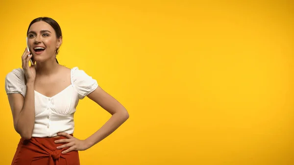 Cheerful brunette model talking on mobile phone isolated on yellow — Stock Photo