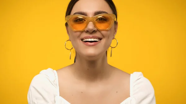 Positive woman in sunglasses looking at camera isolated on yellow — стоковое фото