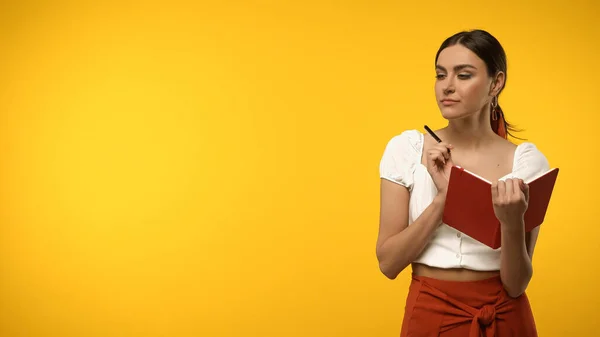 Giovane donna con taccuino e penna isolati su giallo — Foto stock