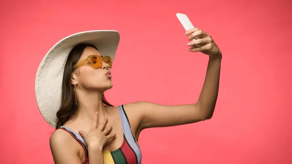 Giovane donna in costume da bagno bronza labbra mentre prende selfie isolato su rosa — Foto stock