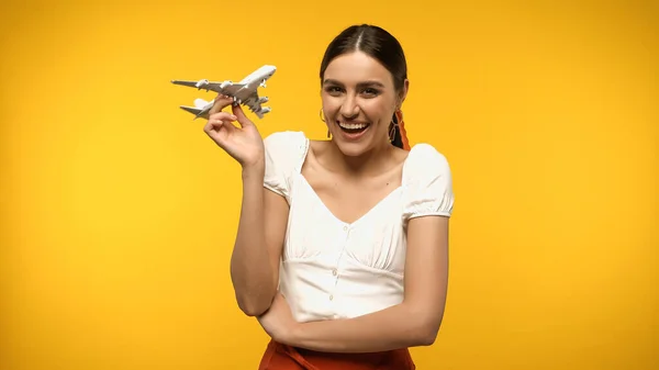 Cheerful woman in blouse holding toy plane isolated on yellow — Stock Photo