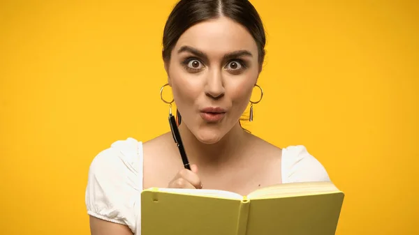 Mujer emocionada sosteniendo pluma cerca del cuaderno aislado en amarillo - foto de stock