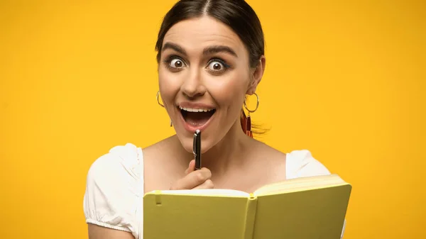 Excited woman in blouse holding pen near notebook isolated on yellow - foto de stock