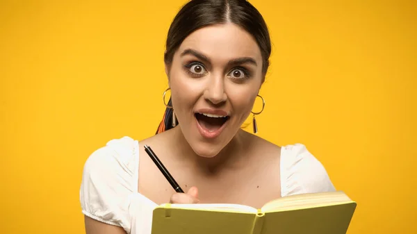 Mujer morena asombrada escribiendo en cuaderno aislado en amarillo - foto de stock