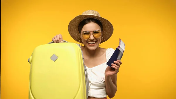 Усміхнений турист у солом'яному капелюсі тримає багаж і паспорт ізольовано на жовтому — стокове фото