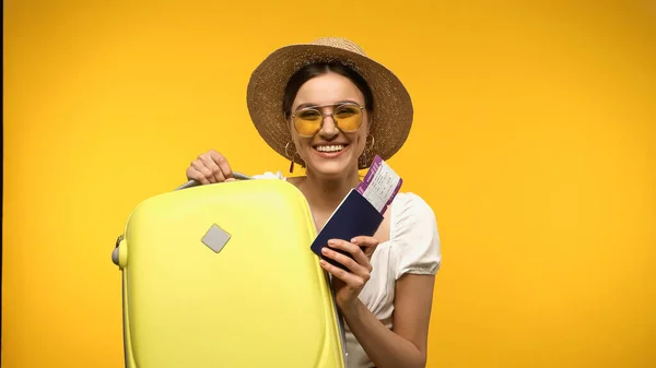 Smiling woman in sunglasses holding suitcase and passport isolated on yellow - foto de stock
