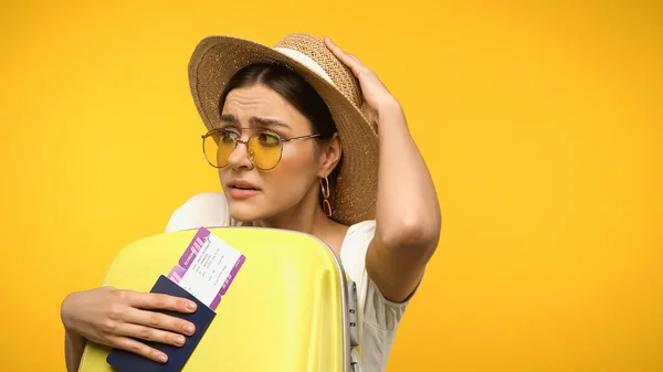 Turista spaventato in occhiali da sole in possesso di passaporto vicino valigia isolato su giallo — Foto stock