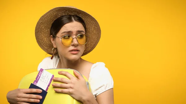 Scared traveler in straw hat hugging suitcase and holding passport isolated on yellow — Fotografia de Stock