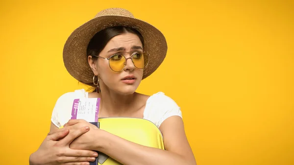 Mujer asustada en gafas de sol con equipaje y pasaporte aislados en amarillo - foto de stock