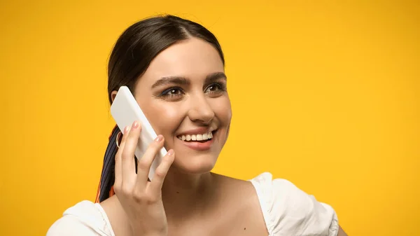 Positive woman talking on mobile phone and looking away isolated on yellow — стоковое фото