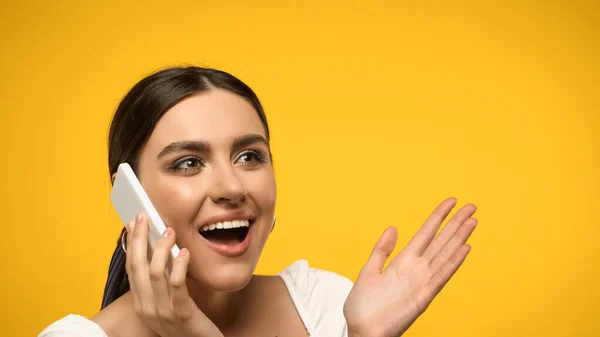 Excited woman in blouse talking on smartphone isolated on yellow — стоковое фото