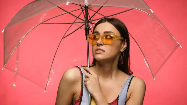 Brünette Frau im Badeanzug hält Regenschirm auf rosa — Stockfoto