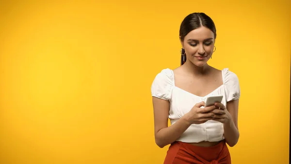Smiling woman in blouse using cellphone isolated on yellow — стоковое фото