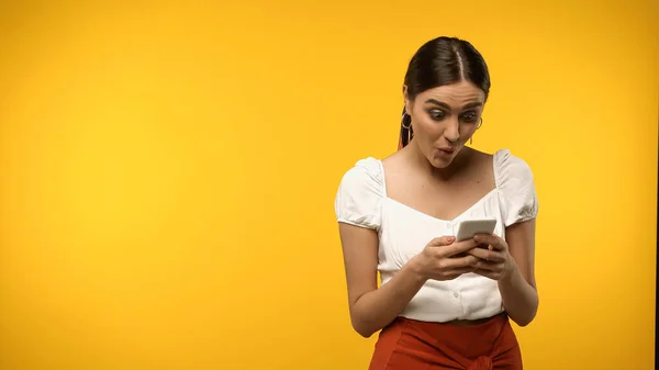 Aufgeregte Frau in weißer Bluse benutzt Handy isoliert auf gelb — Stockfoto