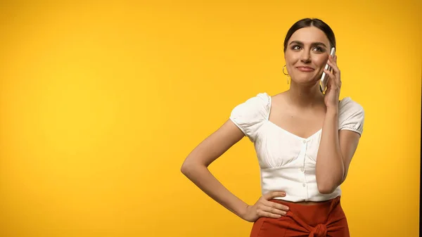 Mujer morena bonita en blusa hablando en el teléfono móvil aislado en amarillo - foto de stock