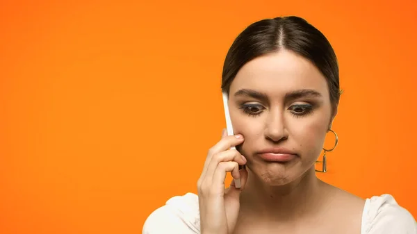 Mujer morena disgustada hablando en smartphone aislado en naranja - foto de stock