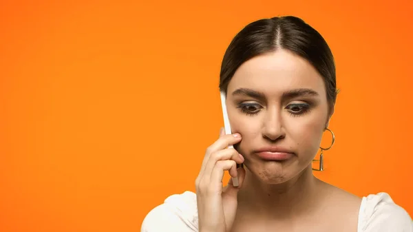 Displeased brunette woman talking on smartphone isolated on orange — Stock Photo