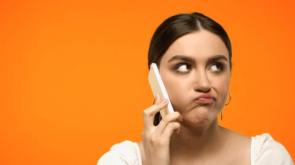 Displeased brunette woman talking on smartphone isolated on orange — Stock Photo