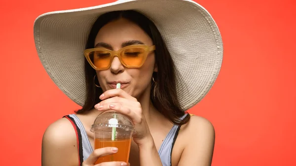 Mulher bonita em óculos de sol e maiô beber coquetel isolado em coral — Fotografia de Stock