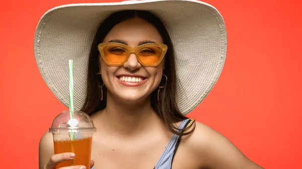 Grazioso modello in cappello di paglia contenente cocktail in bicchiere di plastica isolato su corallo — Foto stock