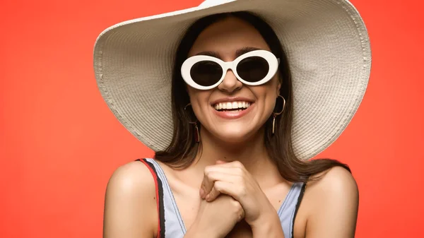 Happy model in sunglasses and straw hat standing isolated on coral — Fotografia de Stock