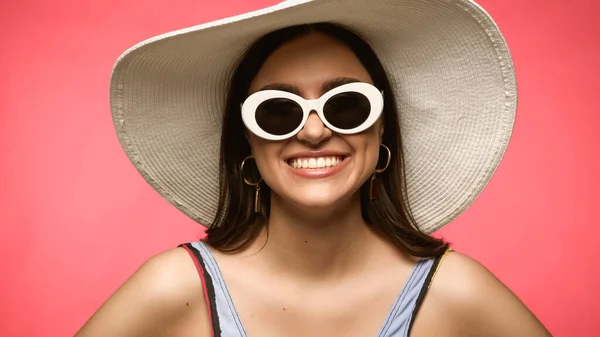 Smiling brunette woman in sunglasses and swimsuit posing isolated on pink — стоковое фото