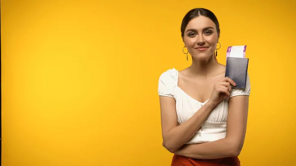 Pretty brunette woman holding passport and air ticket isolated on yellow — Fotografia de Stock