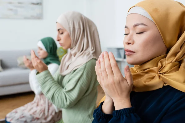 Asian woman praying near blurred muslim daughter and granddaughter at home — Stock Photo