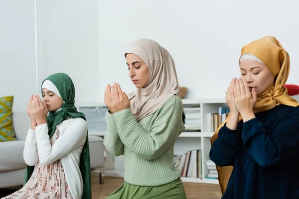 Donne interrazziali in hijab che pregano vicino al bambino a casa — Foto stock