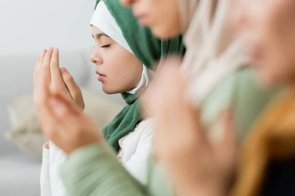 Teen girl praying near blurred women at home — Stock Photo