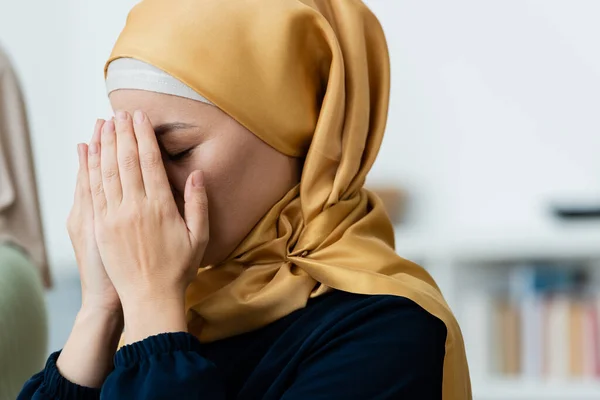 Femme asiatique en hijab couvrant le visage tout en priant à la maison — Photo de stock