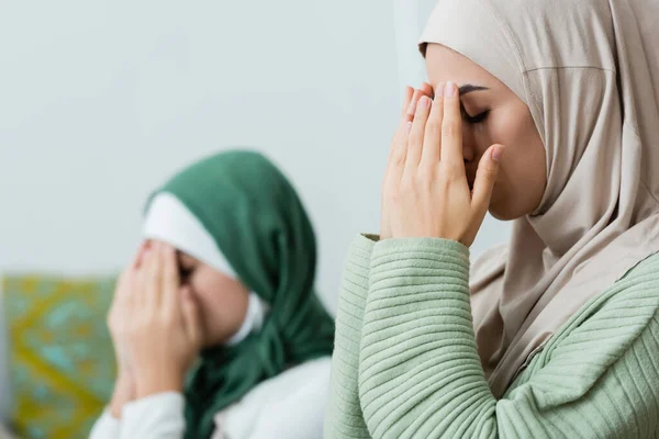Arabo donna che copre il viso mentre prega vicino figlia a casa — Foto stock