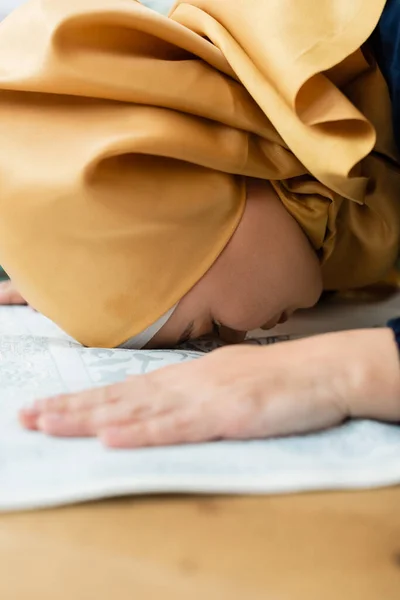 Vista lateral de mujer asiática en hijab rezando en alfombra borrosa - foto de stock