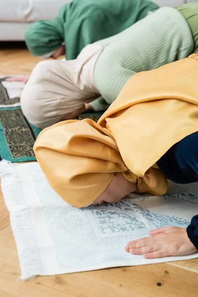 Asian woman bending while praying on rag near muslim family at home — Stock Photo