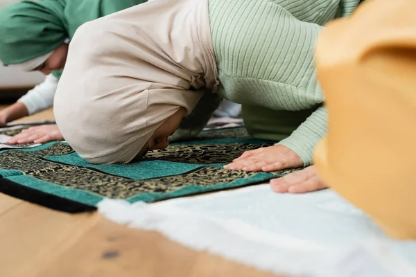 Мусульманская женщина молится и наклоняется на ковре рядом с семьей дома — стоковое фото