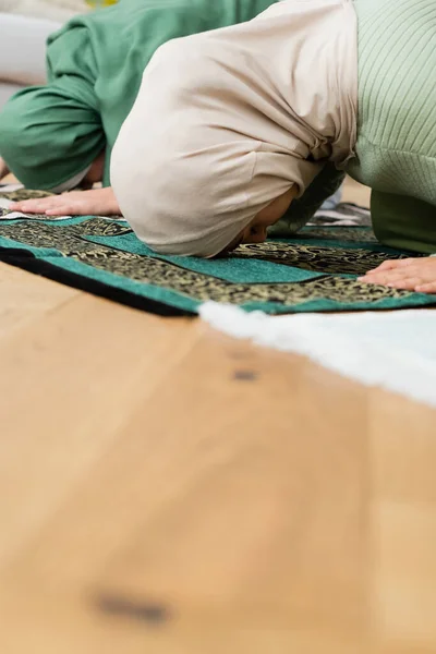 Arabian mother and daughter bending while praying on rugs at home — Stock Photo