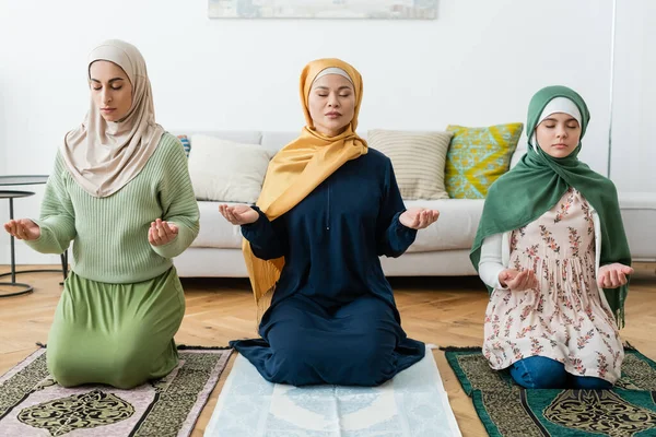 Multiethnic women and teenager praying with closed eyes at home — Stock Photo