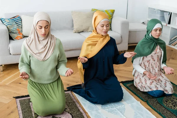 Mulheres multiétnicas e criança orando em tapetes com padrão oriental em casa — Fotografia de Stock