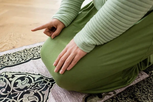 Ausgeschnittene Ansicht einer arabischen Frau, die mit dem Finger zeigt, während sie zu Hause auf Teppich betet — Stockfoto