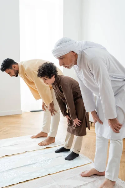 Uomo maturo in piedi su un tappeto vicino alla famiglia araba a casa — Foto stock