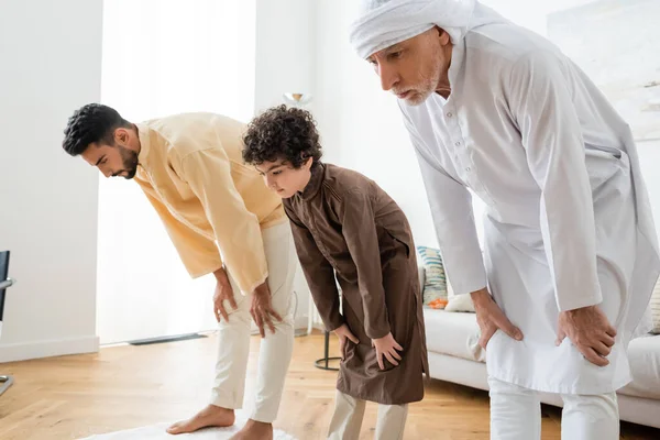 Interracial men and muslim boy bending while praying at home — Stock Photo