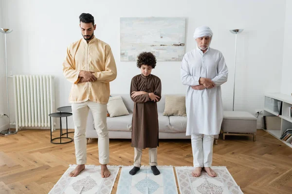 Muslim kid crossing arms while praying near interracial family at home — Stock Photo